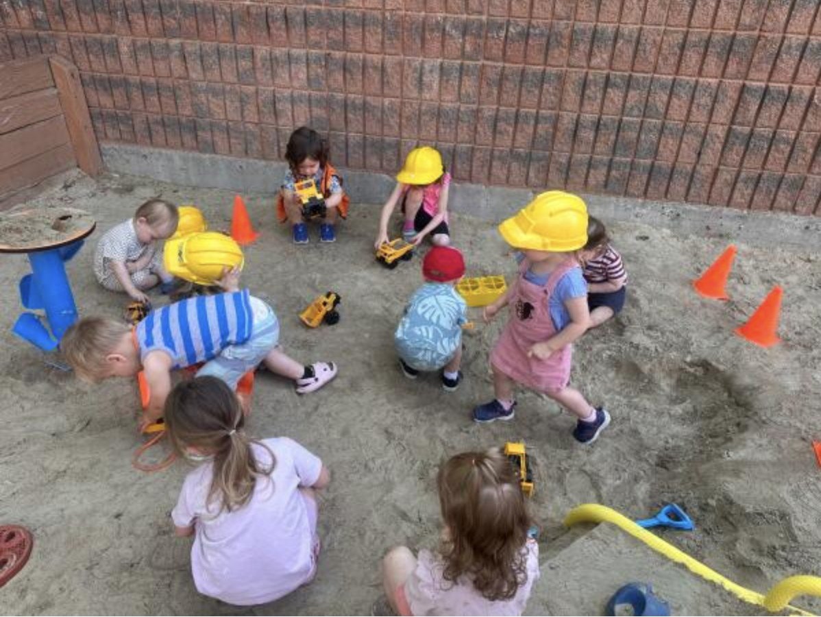 Preschoolers in hard hats digging in the sandbox